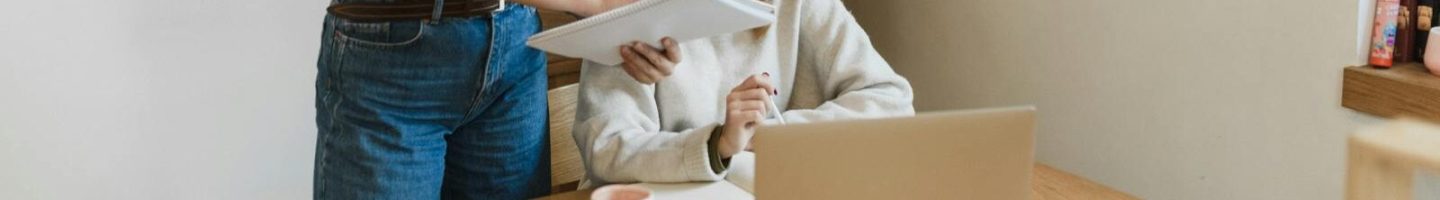 Two women collaborating enthusiastically at a desk with a laptop in a modern office.