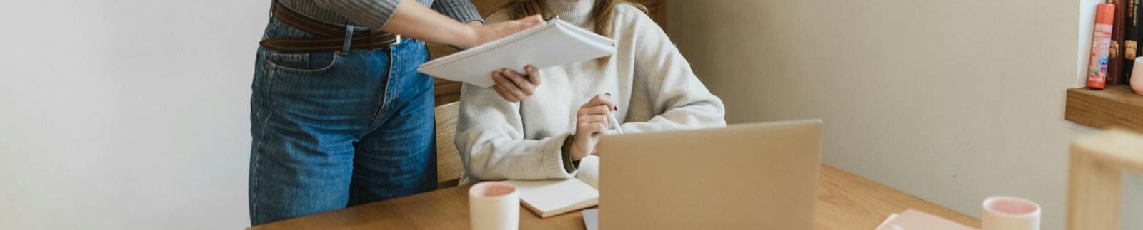 Two women collaborating enthusiastically at a desk with a laptop in a modern office.